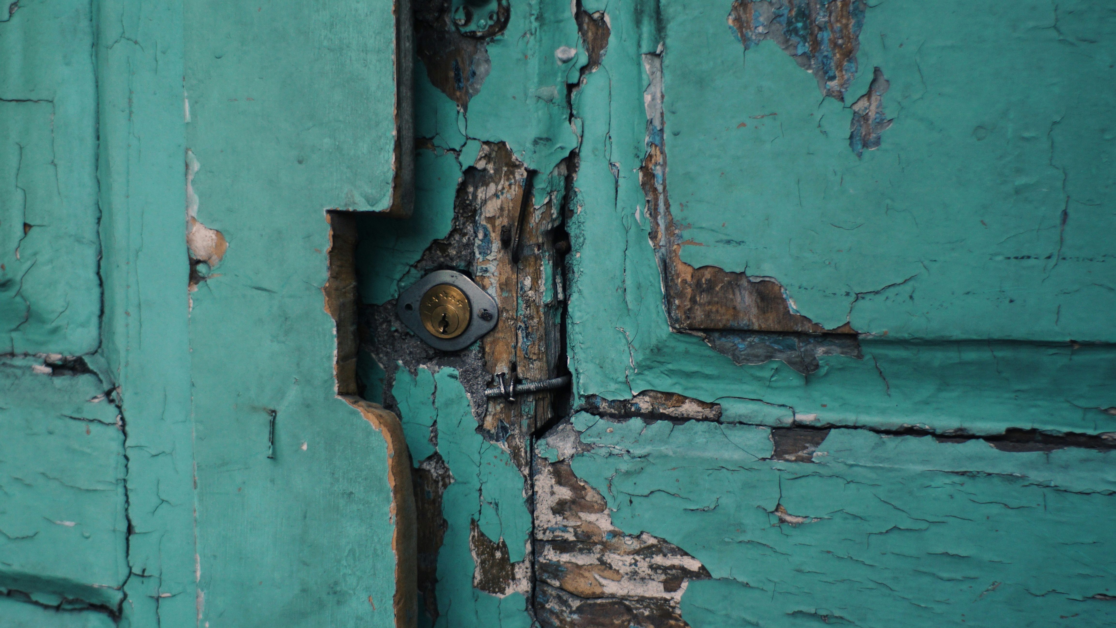 verwitterte Türe mit altem Riegel und neuem Schloss mit meergrünem Lack, der abgeplatzt ist